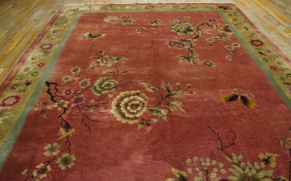 Rose and green floral rug with a thick border lies on distressed wooden floors.