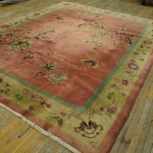 Low-pile pink and green floral rug with fringe lying on rustic wood floorboards.
