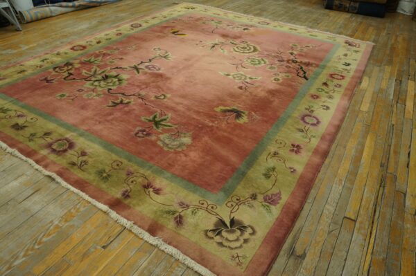 Low-pile pink and green floral rug with fringe lying on rustic wood floorboards.