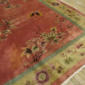 Rose-colored rug with yellow and green botanical patterns, framed by a wide olive green border on wood floors.
