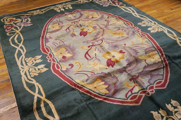 A deep green rug featuring yellow and purple floral designs within a central oval set on wood flooring.