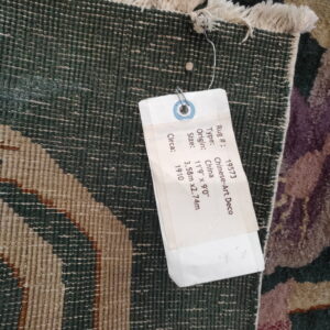 Close-up of a rug's dark green backing and white fringe, with an attached white tag.