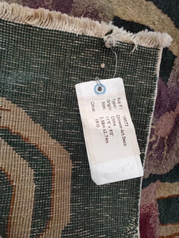 Close-up of a rug's dark green backing and white fringe, with an attached white tag.