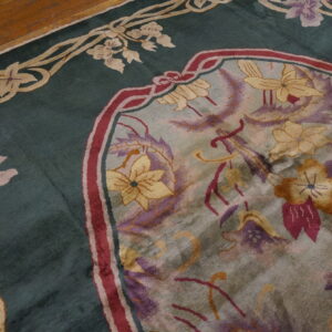 Stylized floral rug in deep teal, cream, and purple accents lying on a brown hardwood floor.