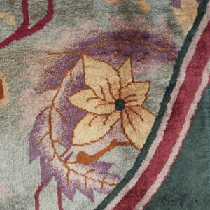Plush rug texture highlights a dense pattern of burgundy, gold, and purple floral motifs on a gray-green field.