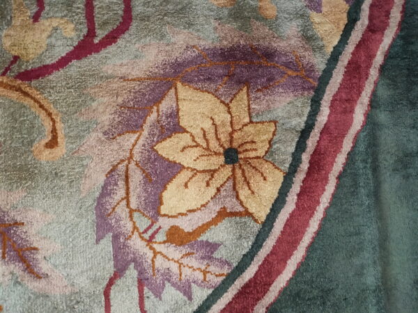 Plush rug texture highlights a dense pattern of burgundy, gold, and purple floral motifs on a gray-green field.