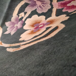 Detailed view of a dark green rug featuring cream, purple, pink, and rust abstract floral motifs.