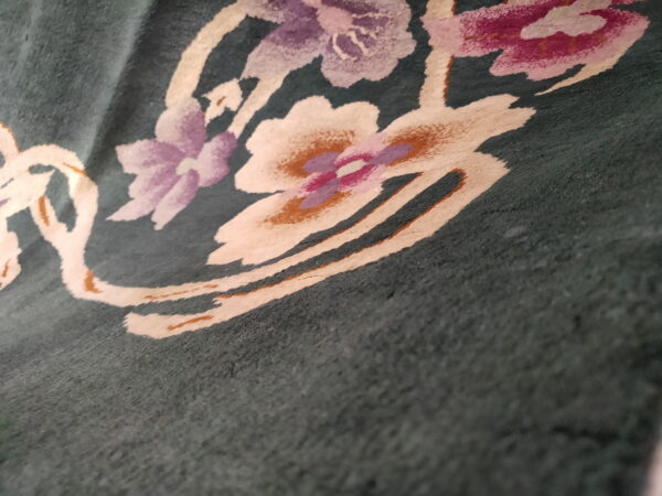 Detailed view of a dark green rug featuring cream, purple, pink, and rust abstract floral motifs.
