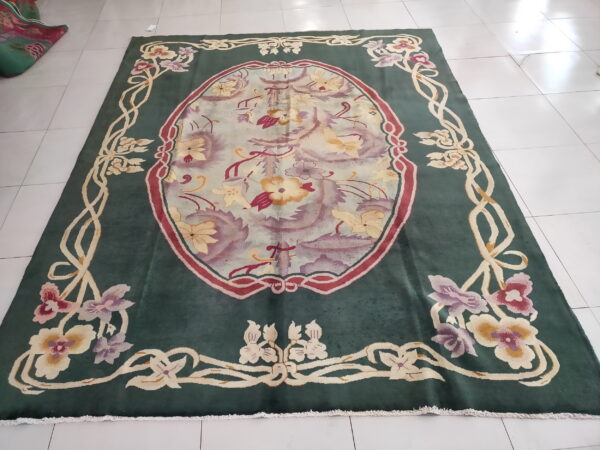 Teal green rug with a pale oval floral medallion and ornate vine border rests on white tiled flooring.