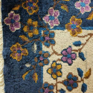 High-pile rug detail with floral vines in purple, gold, and blue on contrasting navy and tan backgrounds.