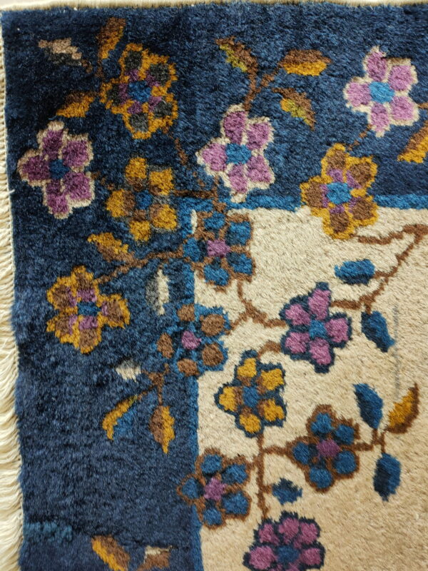 High-pile rug detail with floral vines in purple, gold, and blue on contrasting navy and tan backgrounds.