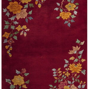 Deep red rug with plush pile, featuring yellow, green, and pink floral clusters along the border.