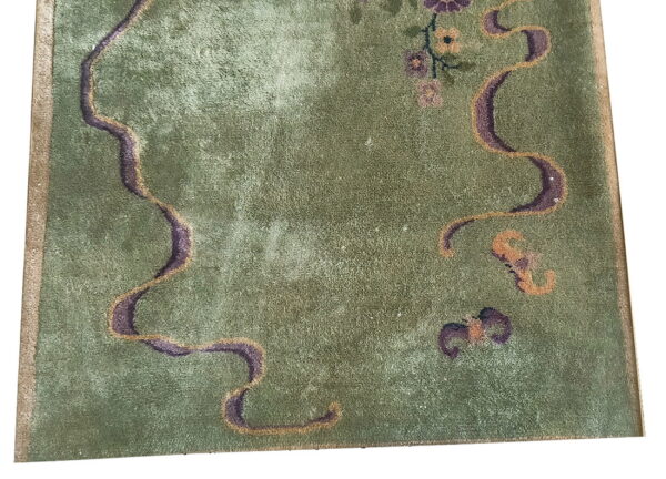 Close up of a green textured rug featuring curving purple and tan borders and floral accents.
