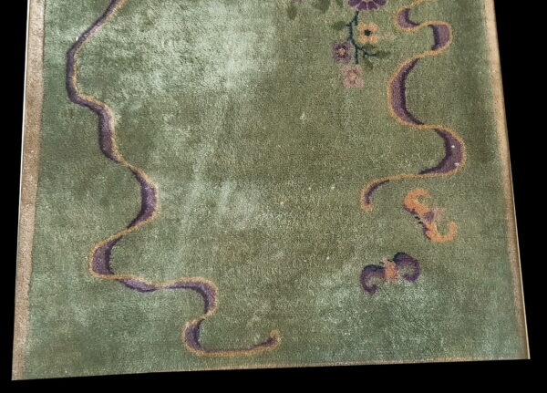 Green low-pile rug detail featuring winding purple and gold lines, small flowers, and a tan border against black.