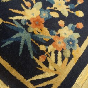 Detailed view of a navy rug featuring muted floral and linear tan patterns next to light, distressed wood flooring.