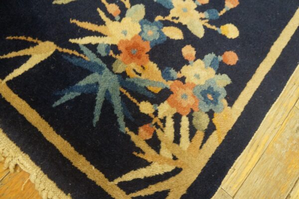 Detailed view of a navy rug featuring muted floral and linear tan patterns next to light, distressed wood flooring.