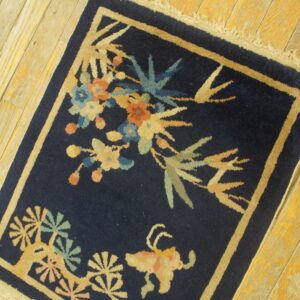 Low-pile navy rug with colorful floral and animal designs framed by a tan border on light wood plank flooring.