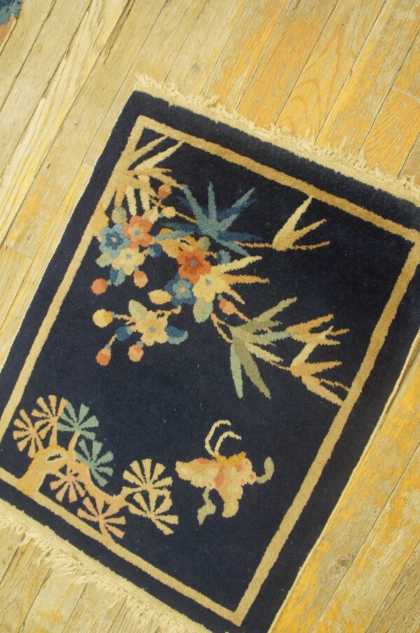 Low-pile navy rug with colorful floral and animal designs framed by a tan border on light wood plank flooring.