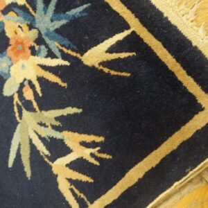 Navy rug with tan border and blue, peach, and sage botanical patterns rests on distressed wood flooring.