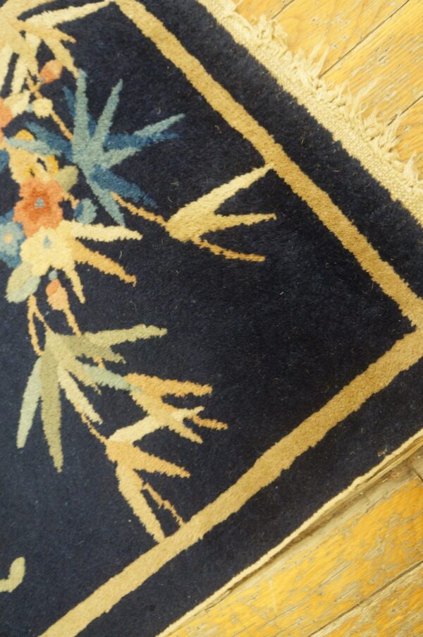 Navy rug with tan border and blue, peach, and sage botanical patterns rests on distressed wood flooring.
