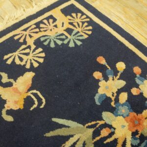 Navy rug featuring cream, yellow, green, and blue floral patterns rests on distressed blonde wood flooring.