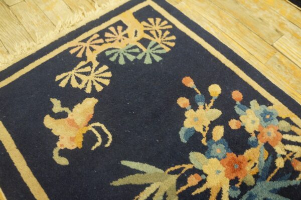 Navy rug featuring cream, yellow, green, and blue floral patterns rests on distressed blonde wood flooring.