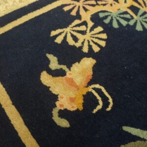 High-pile navy rug featuring a beige border and gold, peach, and green stylized floral patterns.