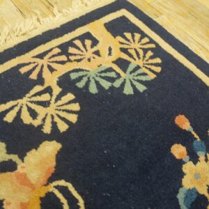 Navy blue rug corner with yellow, pink, and green floral motifs on light wood plank flooring.