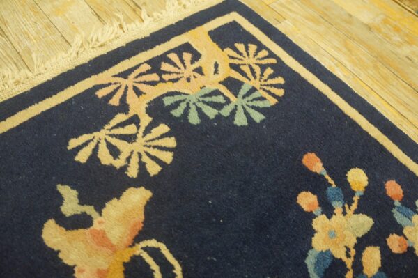 Navy blue rug corner with yellow, pink, and green floral motifs on light wood plank flooring.