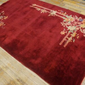 Burgundy area rug with pastel floral motifs and parallel pink stripes lies on rustic plank wood floor.