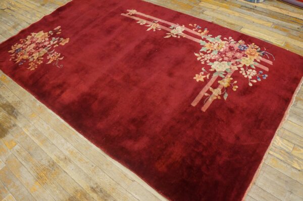 Burgundy area rug with pastel floral motifs and parallel pink stripes lies on rustic plank wood floor.