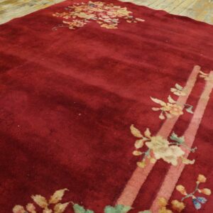 Deep red cut pile rug with gold and pink floral designs and broad stripes on light wood flooring.