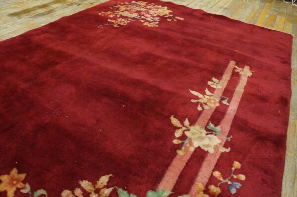 Deep red cut pile rug with gold and pink floral designs and broad stripes on light wood flooring.