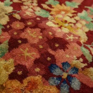 Plush red rug featuring a dense pattern of yellow, pink, blue, and green floral motifs.