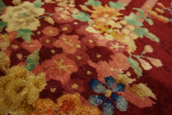 Plush red rug featuring a dense pattern of yellow, pink, blue, and green floral motifs.