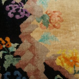 Plush beige rug with colorful abstract floral motifs, including purple and orange, next to worn wood planks.