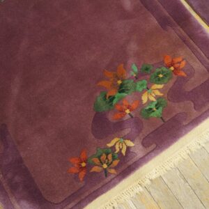 Deep purple high-pile rug featuring carved orange and green flowers on distressed wood plank flooring.
