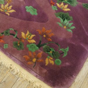Corner view of a plush purple rug with sculpted orange and green floral designs on light wood flooring.