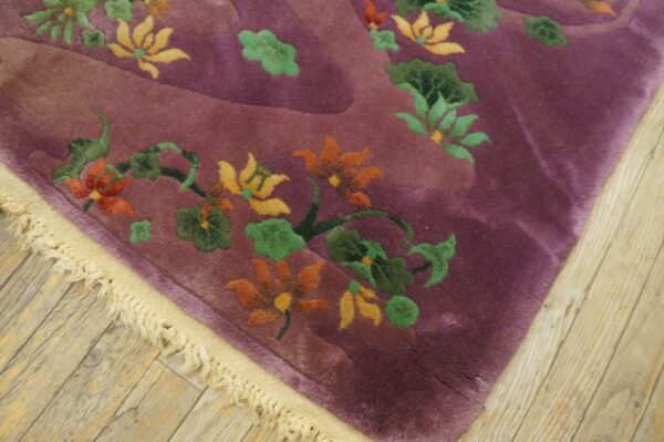 Corner view of a plush purple rug with sculpted orange and green floral designs on light wood flooring.