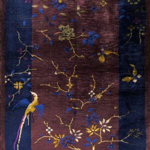Navy and burgundy rug featuring colorful branches, flowers, and a stylized bird motif.