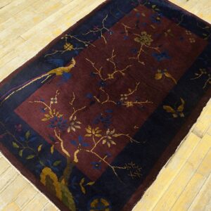 Low-pile burgundy and navy rug with a bird and floral pattern lies on distressed yellow wood planks.