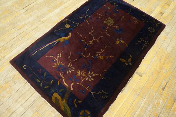 Low-pile burgundy and navy rug with a bird and floral pattern lies on distressed yellow wood planks.