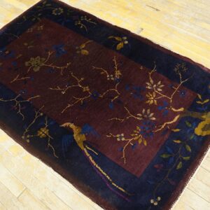 Burgundy field rug with navy border, featuring gold botanical and bird designs on light wood planks.