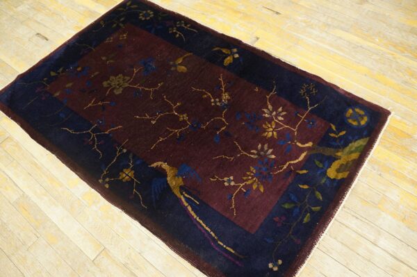 Burgundy field rug with navy border, featuring gold botanical and bird designs on light wood planks.