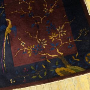 A low pile navy and maroon pictorial rug depicting a gold bird and flowering branches on distressed wood flooring.