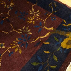 Maroon and navy rug showing a close-up of the yellow and blue floral vine pattern and border on wood planks.