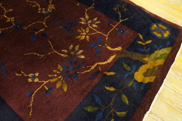 Maroon and navy rug showing a close-up of the yellow and blue floral vine pattern and border on wood planks.
