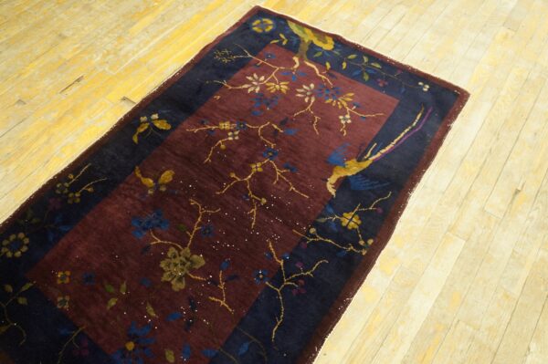 Burgundy and navy runner with floral and bird patterns rests on a distressed light yellow wood floor.
