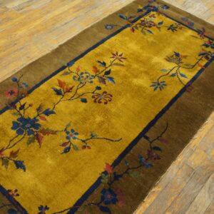 A gold runner rug with colorful floral vines and a brown border rests on distressed wood flooring.
