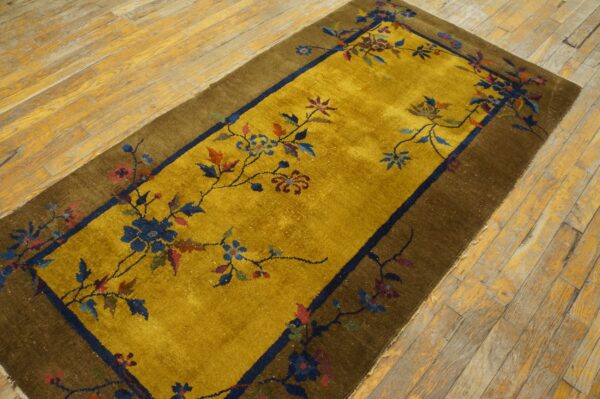 A gold runner rug with colorful floral vines and a brown border rests on distressed wood flooring.